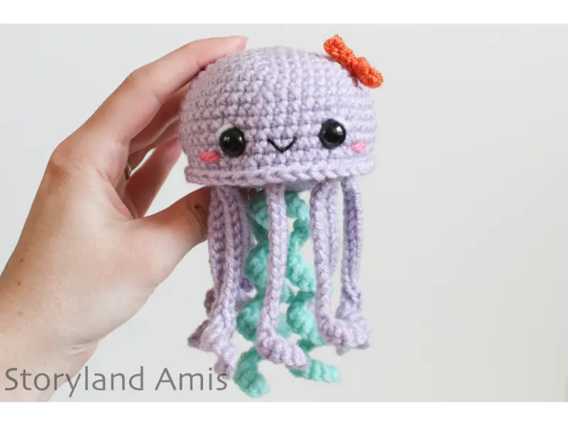 A hand holds a purple and mint green amigurumi jellyfish.