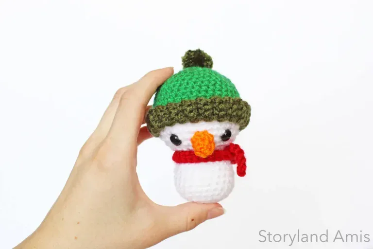 A hand holds up a small crocheted snowman