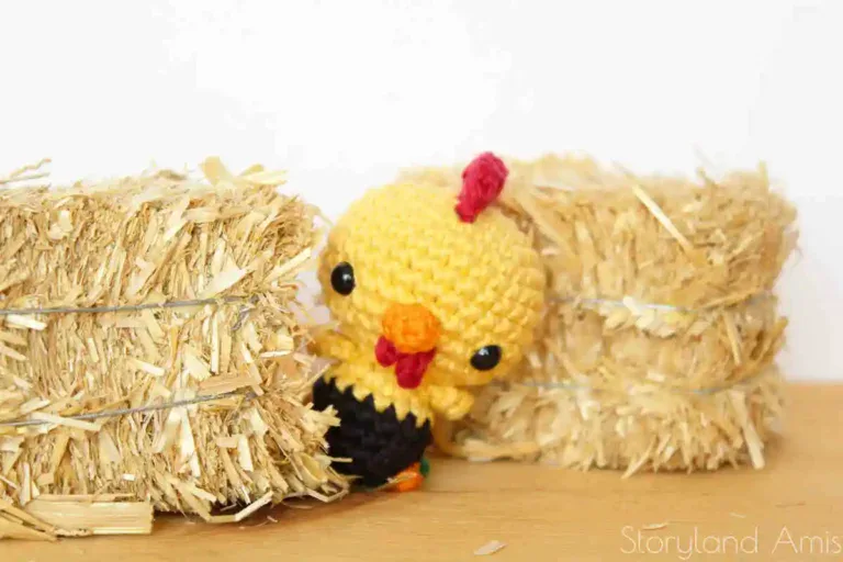 An amigurumi rooster peeks out from behind two mini hay bales.