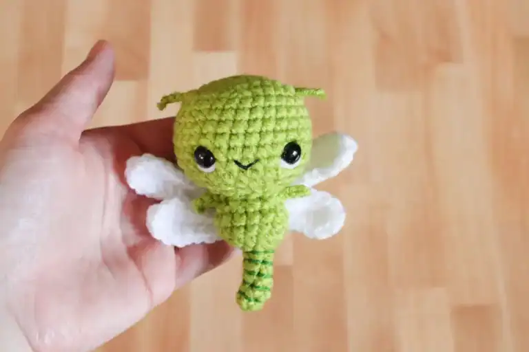 A hand holds a crocheted amigurumi dragonfly