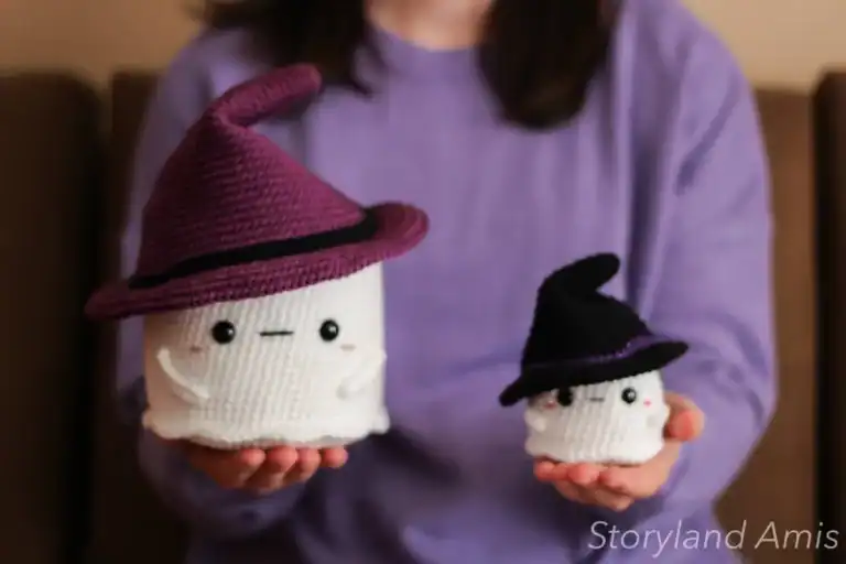 A girl wearing a purple sweater holds up two crocheted ghosts.