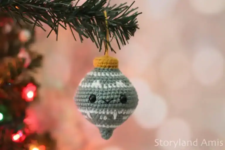 A crocheted Christmas ornament hangs from a faux pine tree branch.