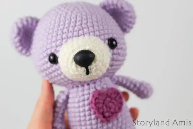 A hand holds up a purple amigurumi bear.