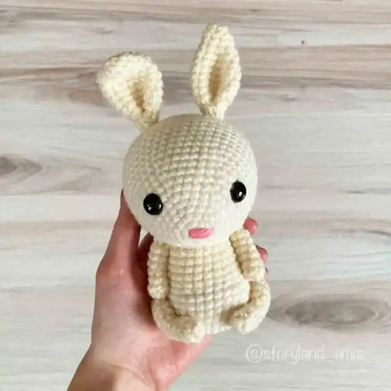 A hand holds up a cream colored amigurumi bunny.