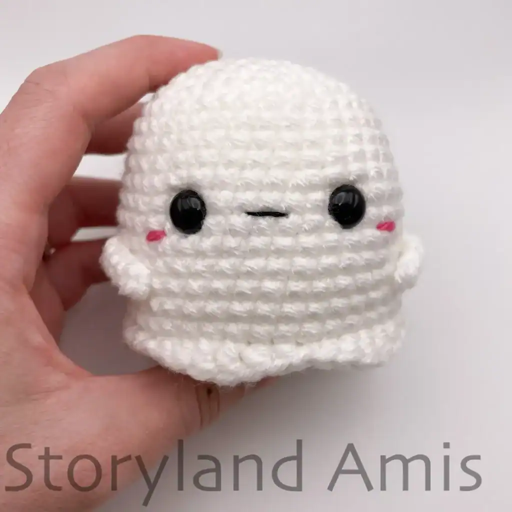 A hand holds a completed amigurumi baby ghost.