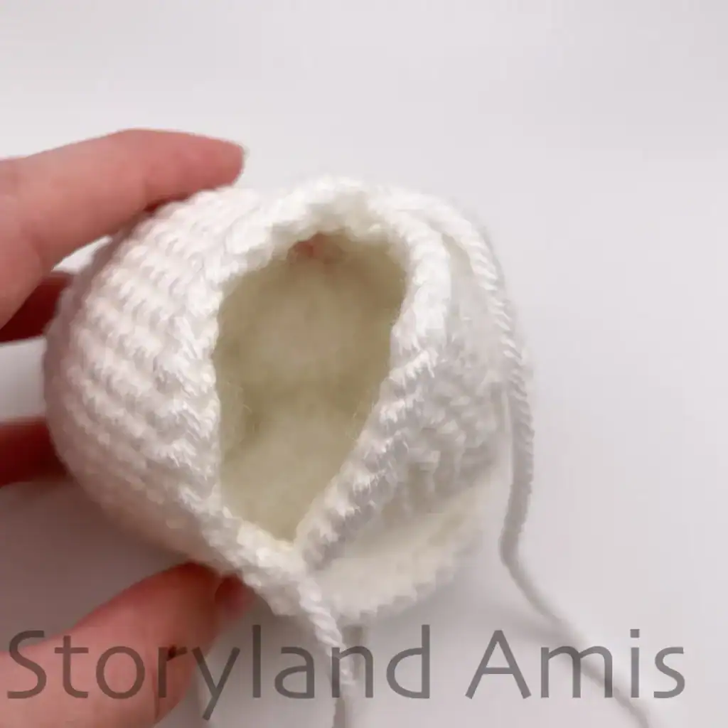 The open bottom edge of a partially finished amigurumi ghost filled with PolyFil stuffing.