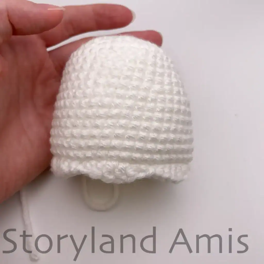 A hand holds a partially finished amigurumi ghost.