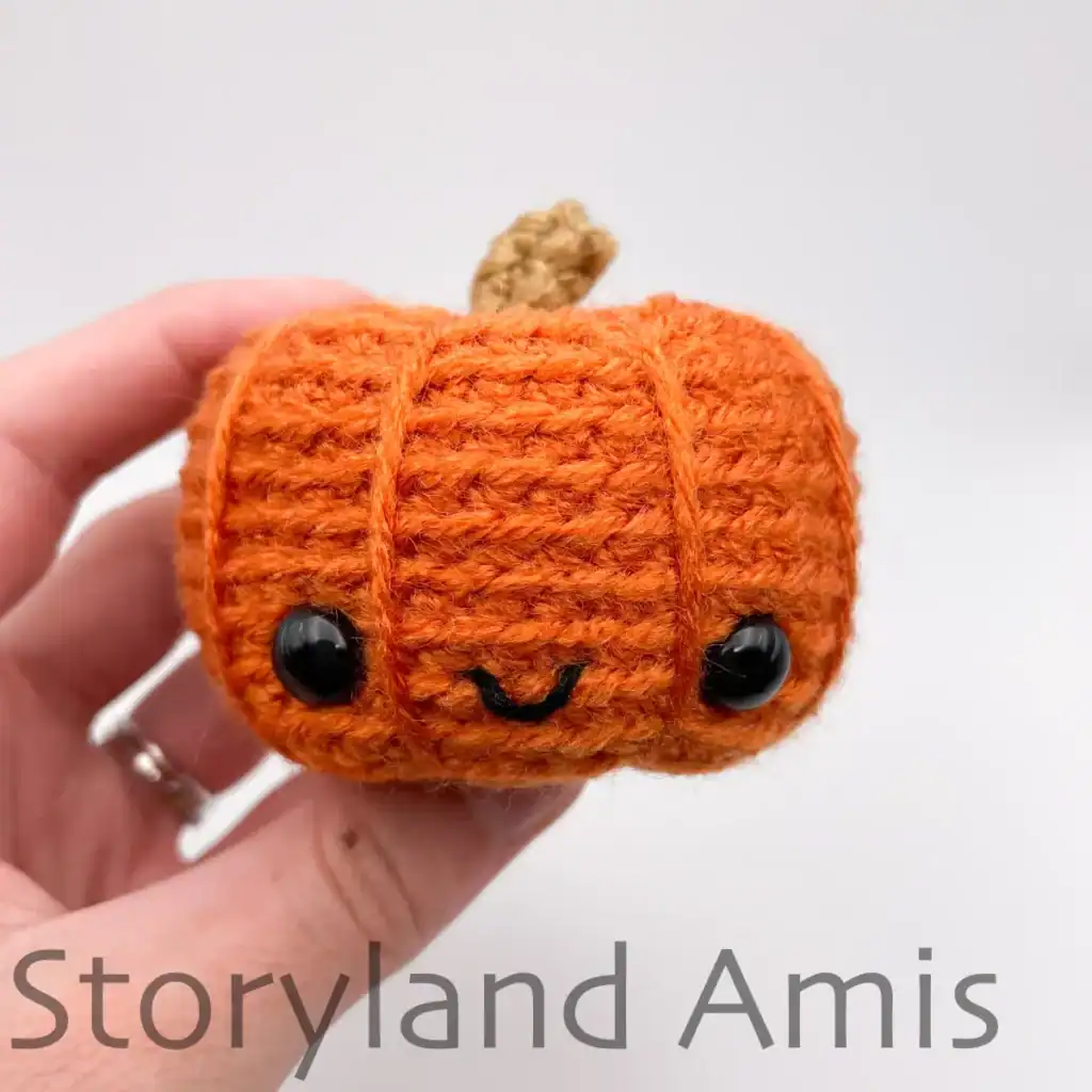 A hand holds up an orange amigurumi pumpkin.