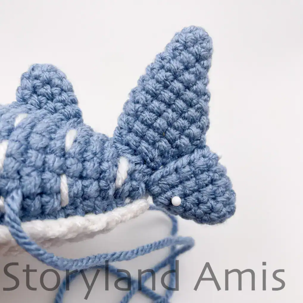 A crocheted whale shark's tail fin is shown from the side.