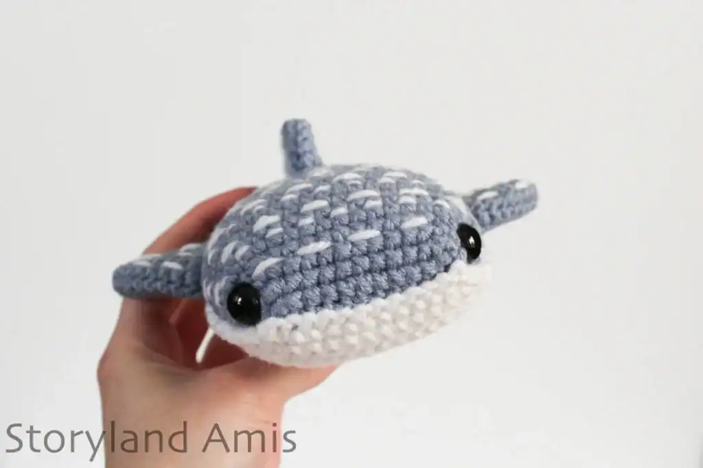 A hand holds up a crocheted whale shark.