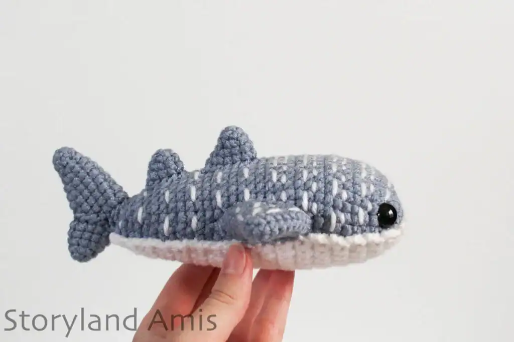 A hand holds up a crocheted whale shark.