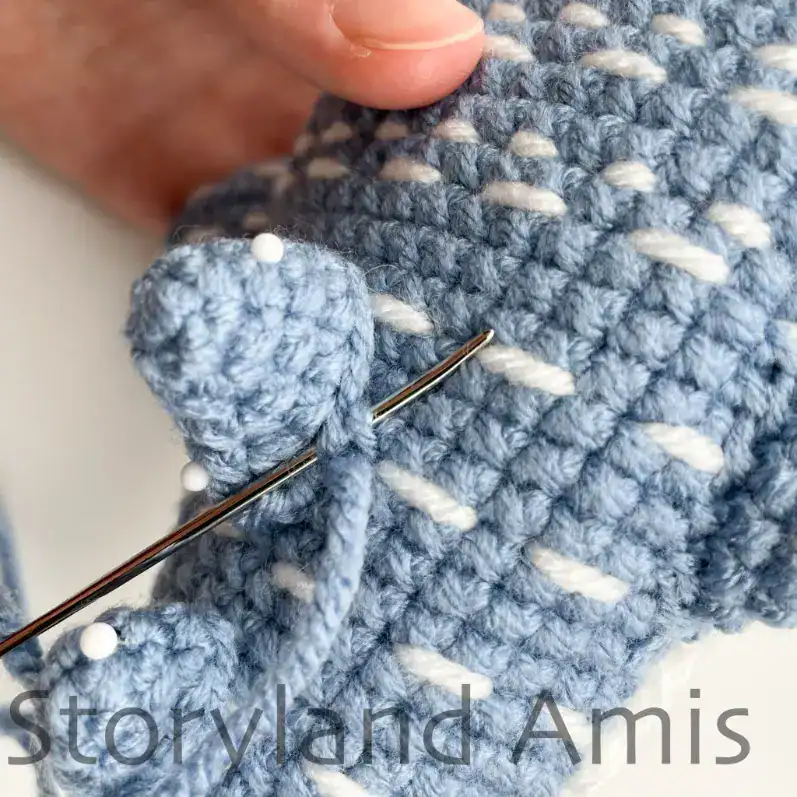 A hand demonstrates how to sew the back fins to the body of an amigurumi whale shark.