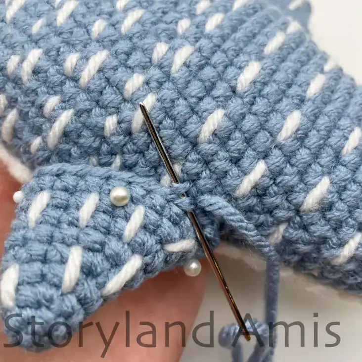 A hand demonstrates how to sew the fins to the body of an amigurumi whale shark.