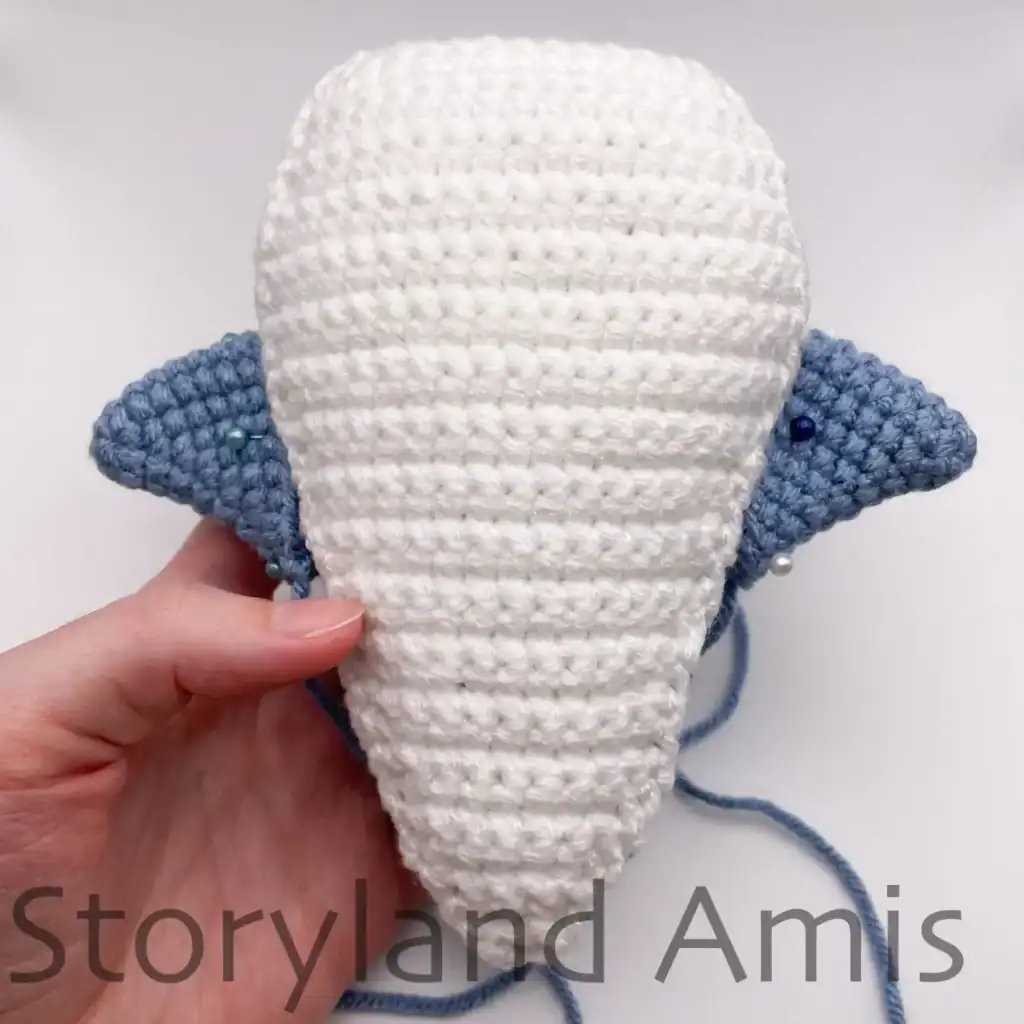A hand holds a partially finished amigurumi whale shark, showing where to place the fins.