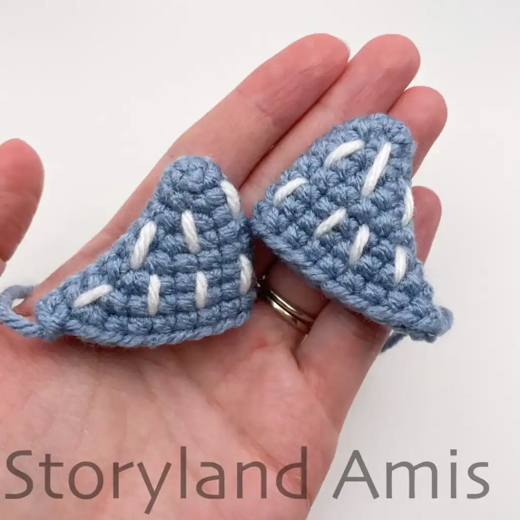A hand holds two crocheted whale shark fins.