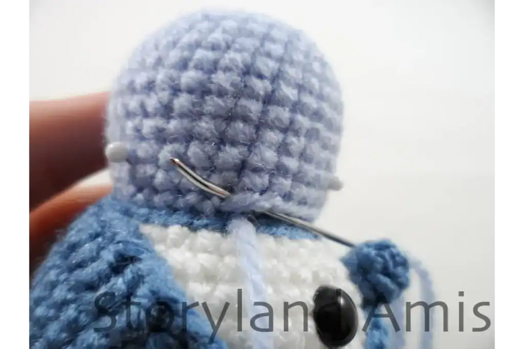 A close-up of a penguin amigurumi, held upside down as the body is sewn to the head using a tapestry needle.
