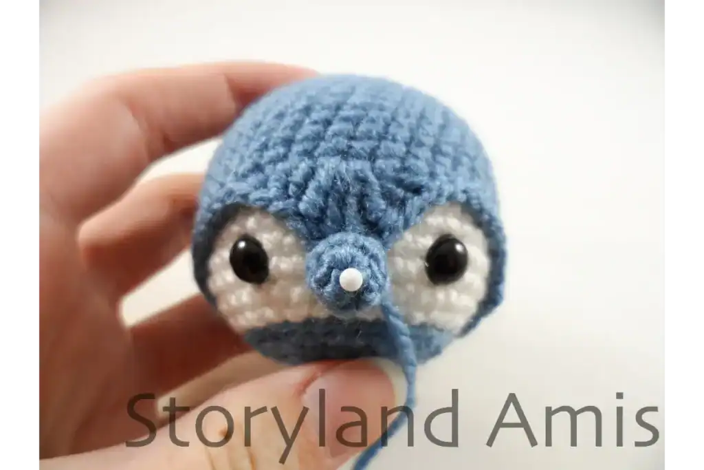 A hand holds up a partially finished amigurumi penguin head.