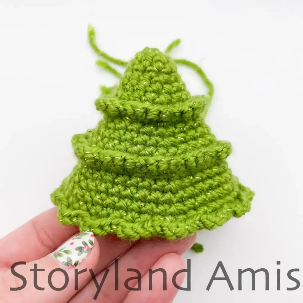 A hand holds a partially finished crocheted mini Christmas tree.