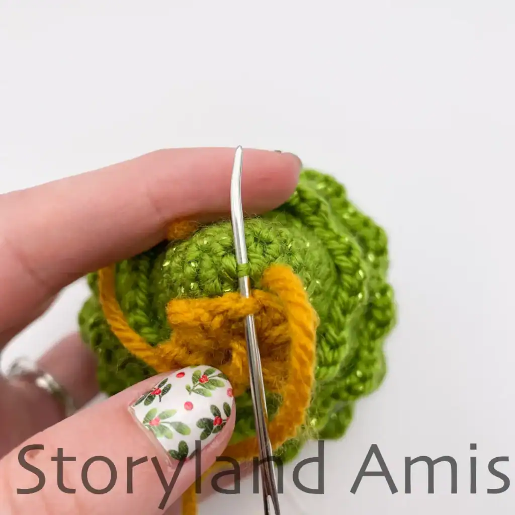 A hand demonstrates how to sew a star to the top of a mini amigurumi Christmas tree.