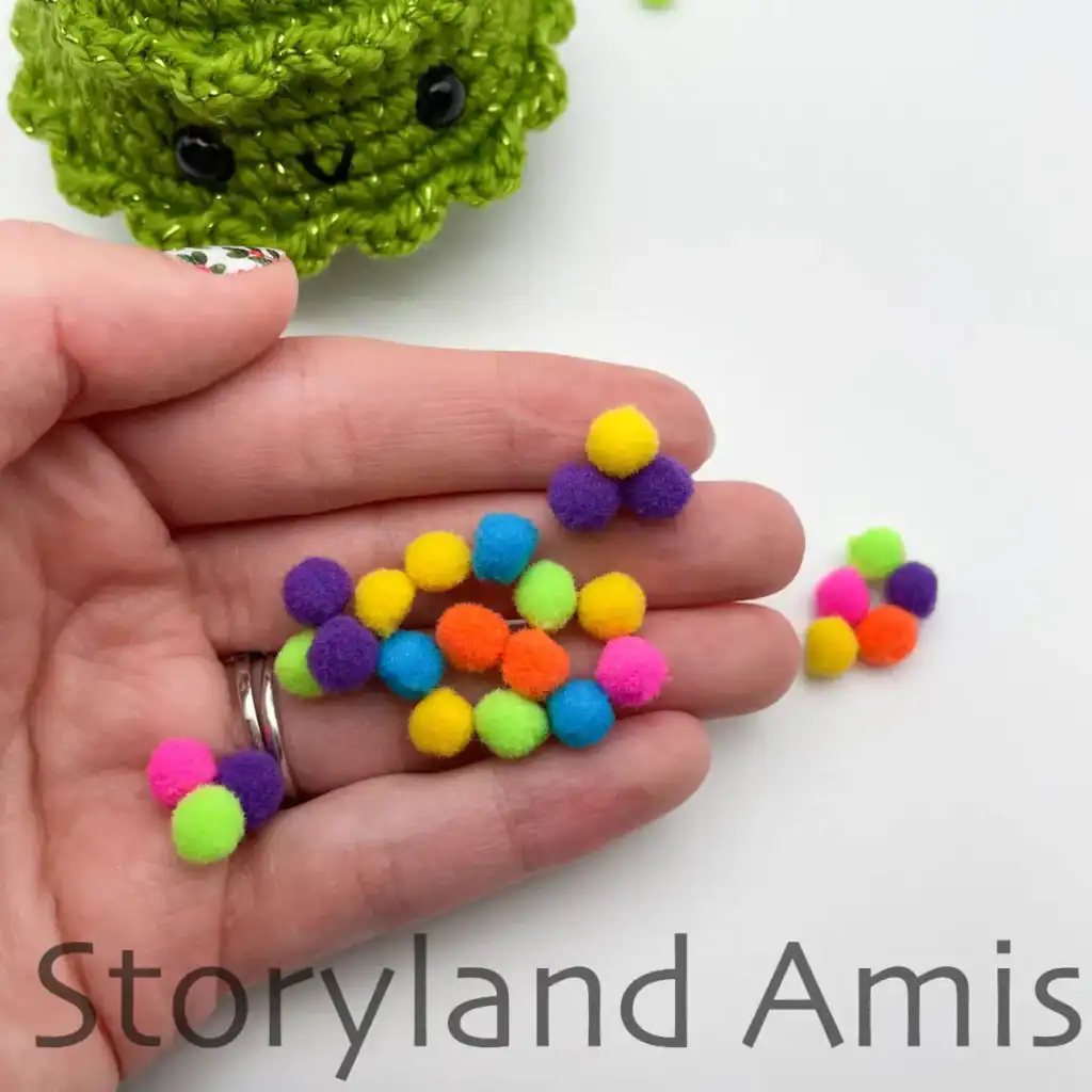 A hand holds a bunch of mini pom poms in various colors.