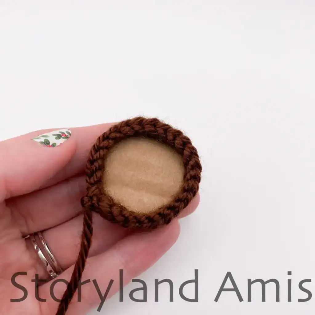 A hand holds a crocheted Christmas tree trunk with a cardboard circle inside the bottom.