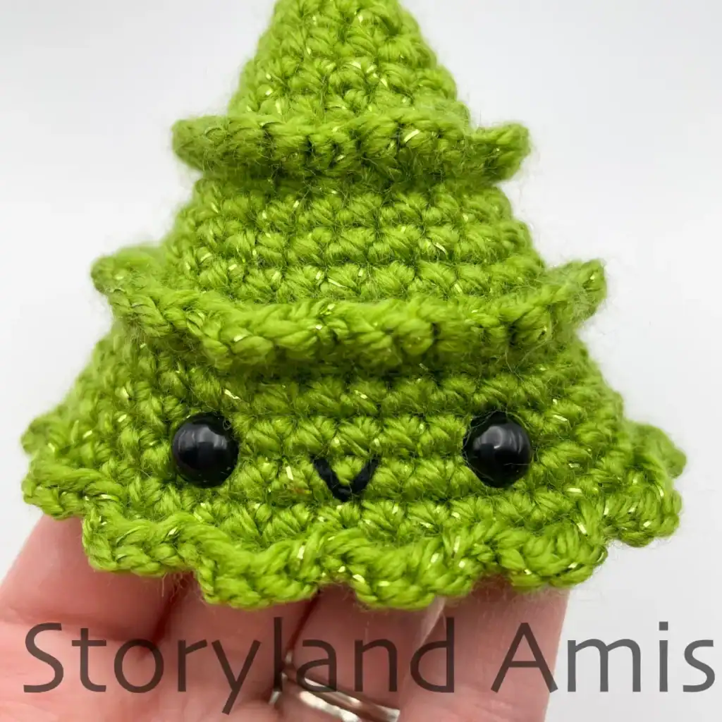 A close-up of an amigurumi Christmas tree's face showing the embroidered mouth and plastic safety eyes.