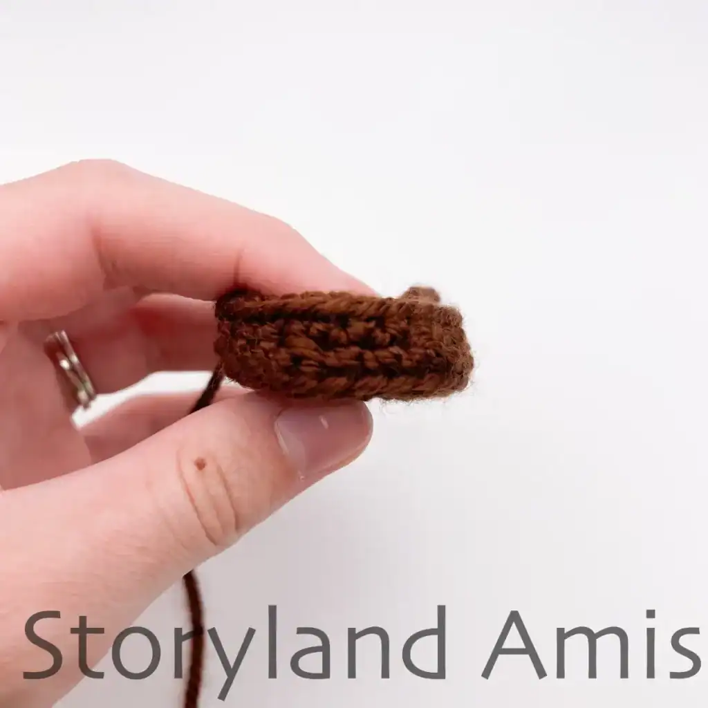 A hand holds up a brown, crocheted trunk for an amigurumi Christmas tree.