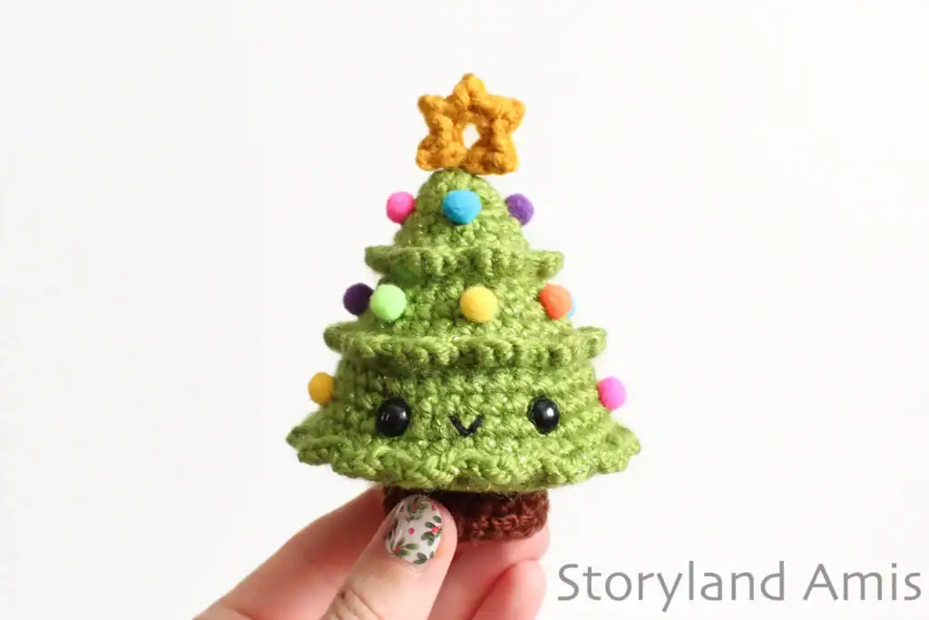 A hand holds up a mini Christmas tree amigurumi.