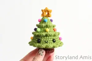 A hand holds up a mini Christmas tree amigurumi.