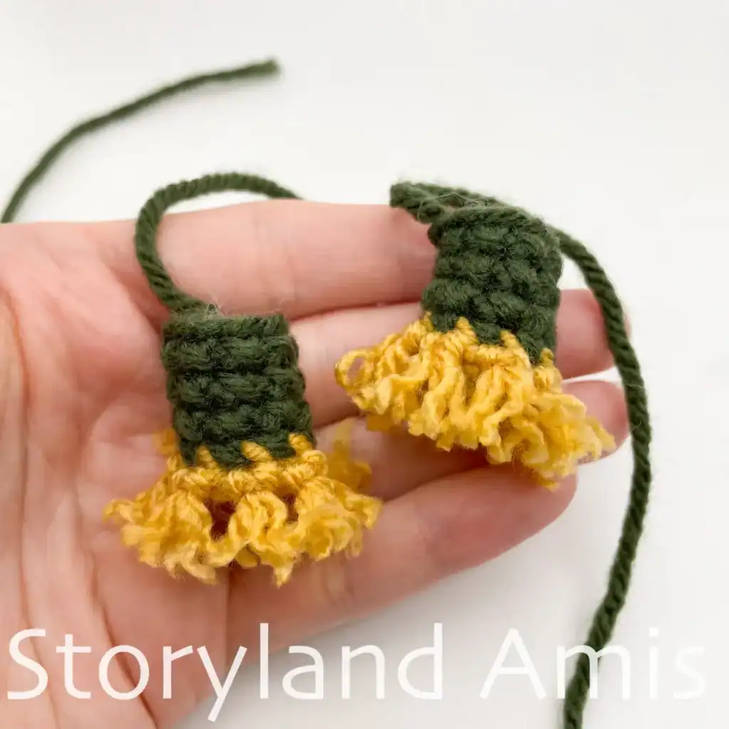 A hand holds two crocheted arms with the fringe added to the ends for an amigurumi scarecrow.