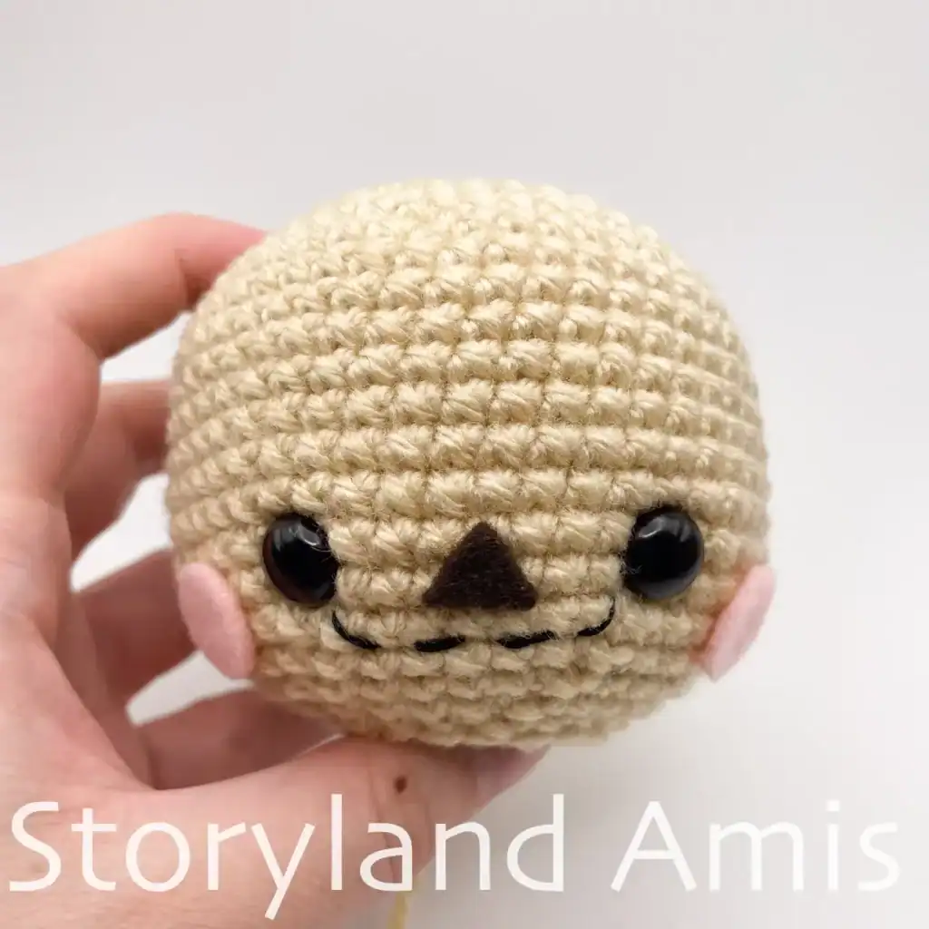 A hand holds a finished amigurumi scarecrow head.