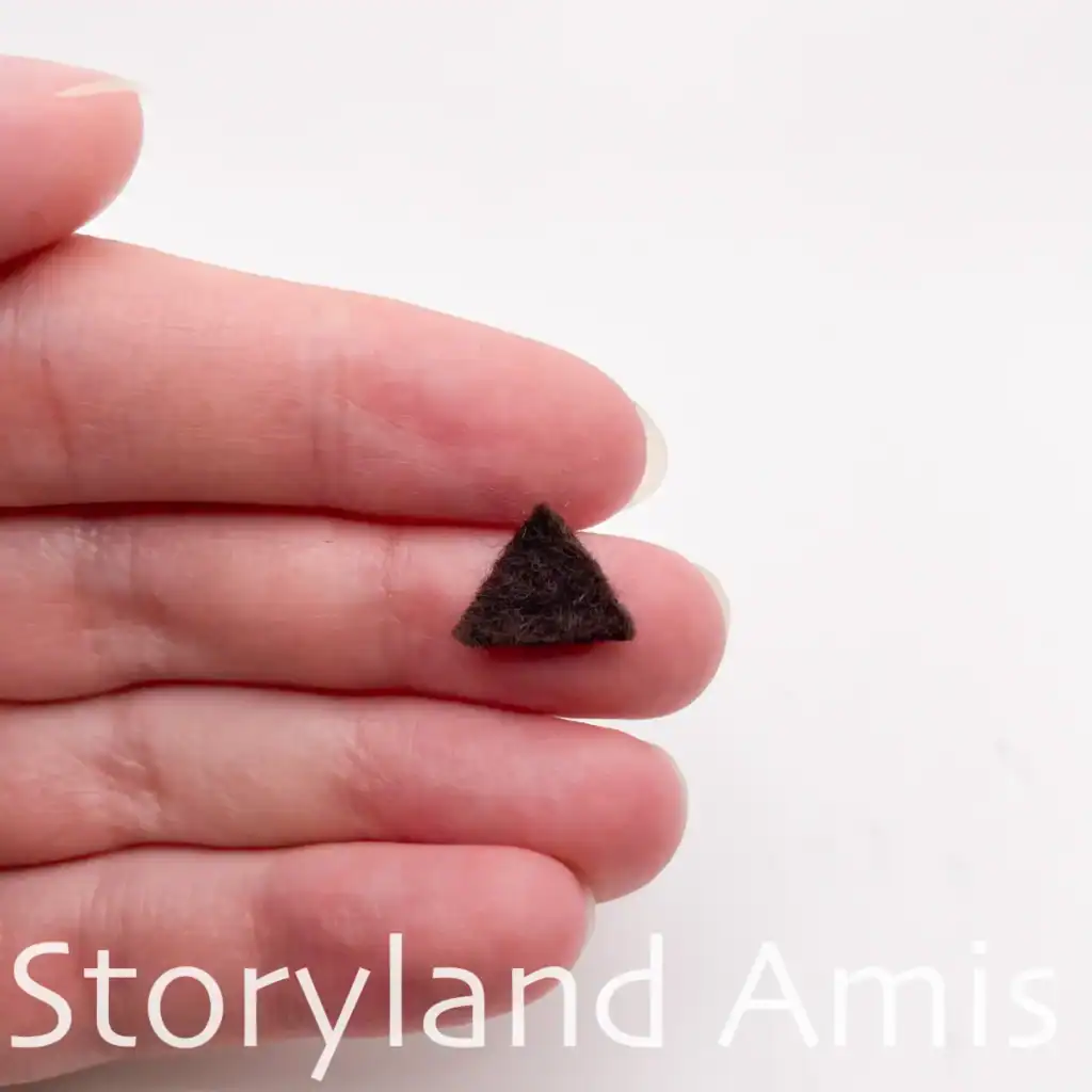 A hand holds a small triangle of brown felt.