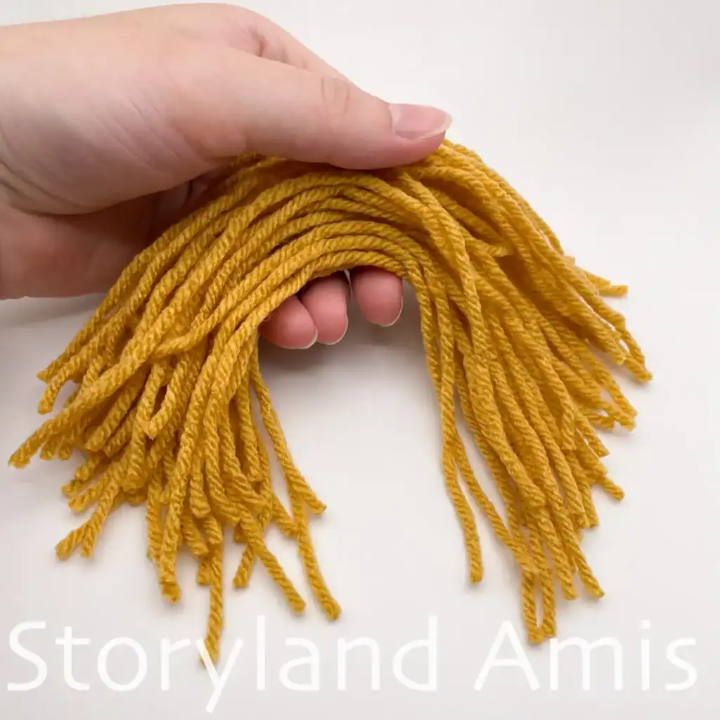 A hand holds a handful of short yarn ends intended for an amigurumi scarecrow.
