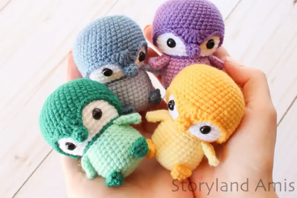 Two hands hold four colorful amigurumi penguins.