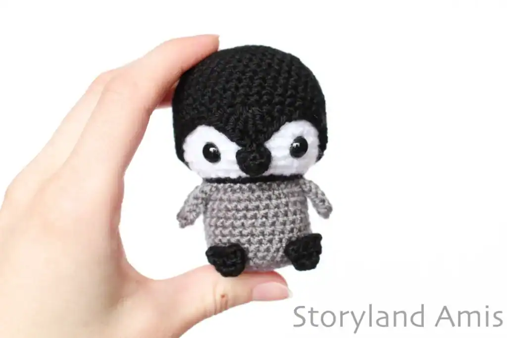 A hand holds up an amigurumi baby penguin.