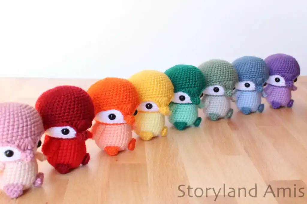 A row of colorful crocheted baby penguins sit on a wooden table.