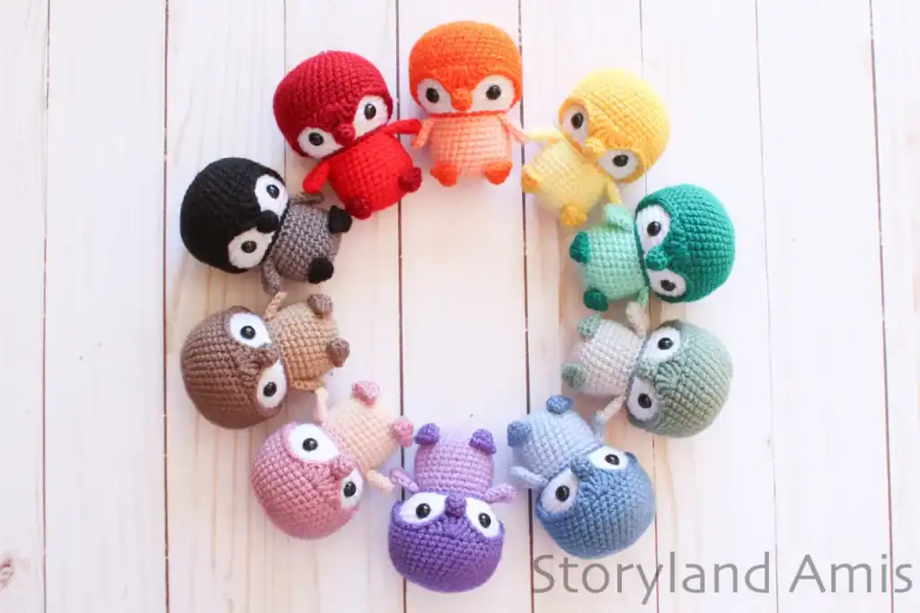 Ten baby amigurumi penguins in a rainbow of colors are arranged in a circle on a wooden table.