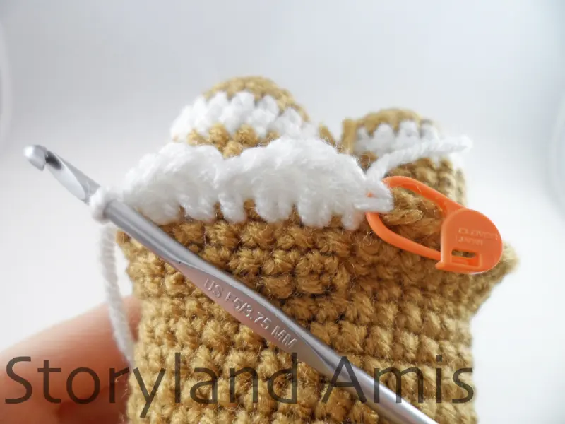 A close-up of a skirt being crocheted around the body of an amigurumi gingerbread girl using an aluminum crochet hook.