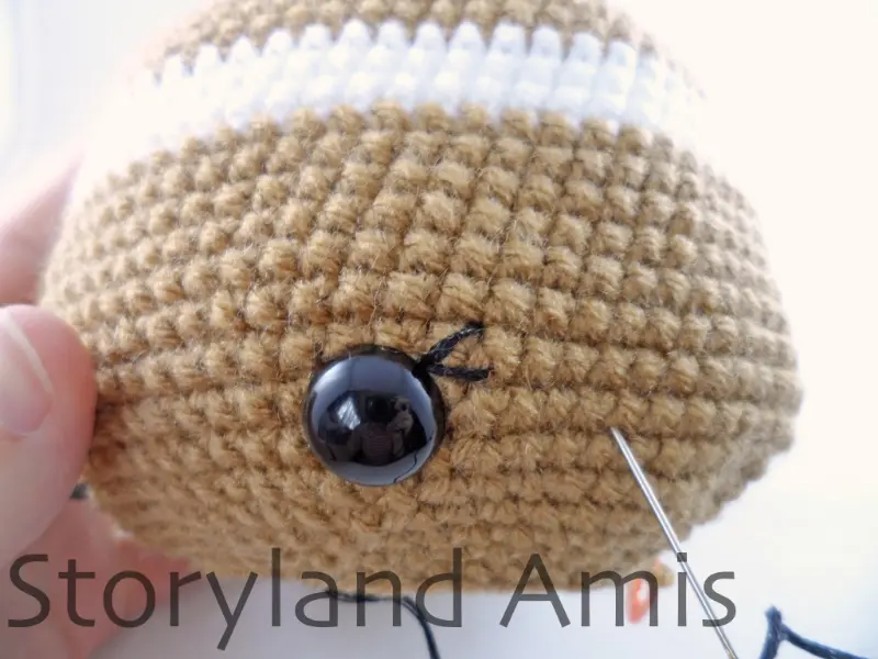 A close-up of the eye on a gingerbread girl amigurumi showing the embroidered eyelashes.