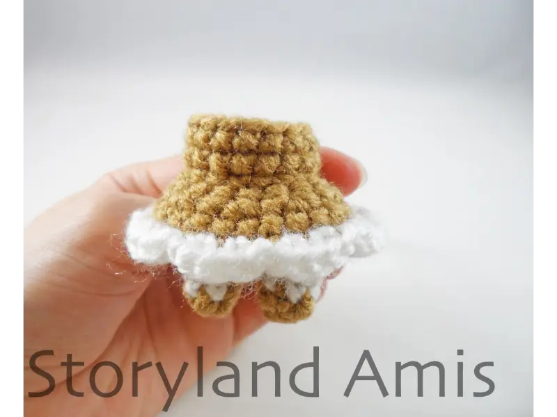 A hand holds up a crocheted body for an amigurumi gingerbread girl.