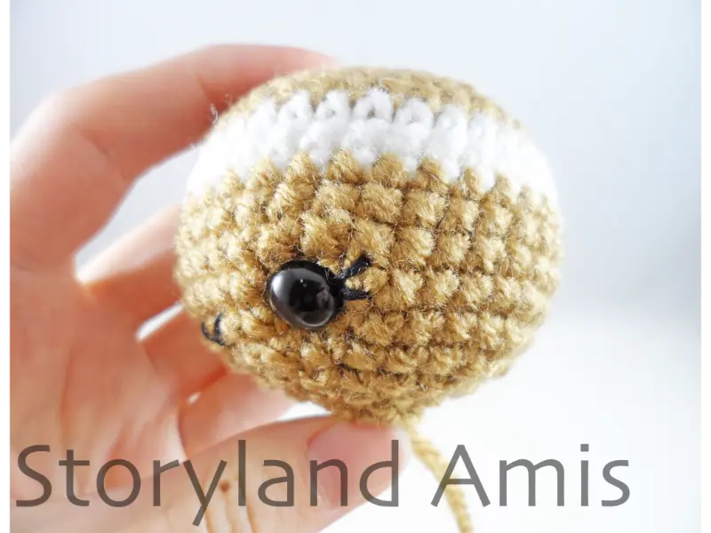 A hand holds a crocheted gingerbread girl head shown from the side.