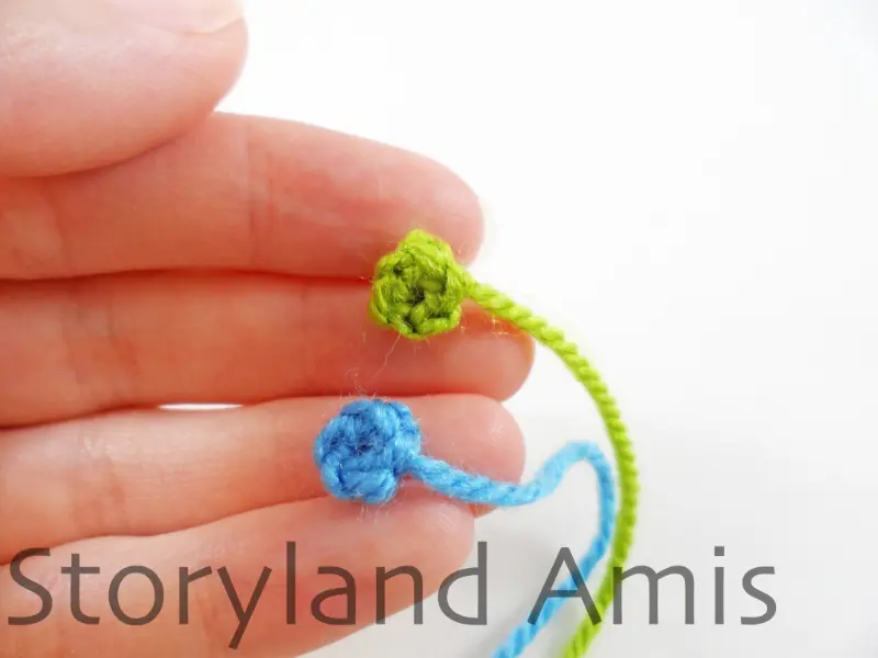 A hand holds two small crocheted circles. One circle is green and the other is blue.