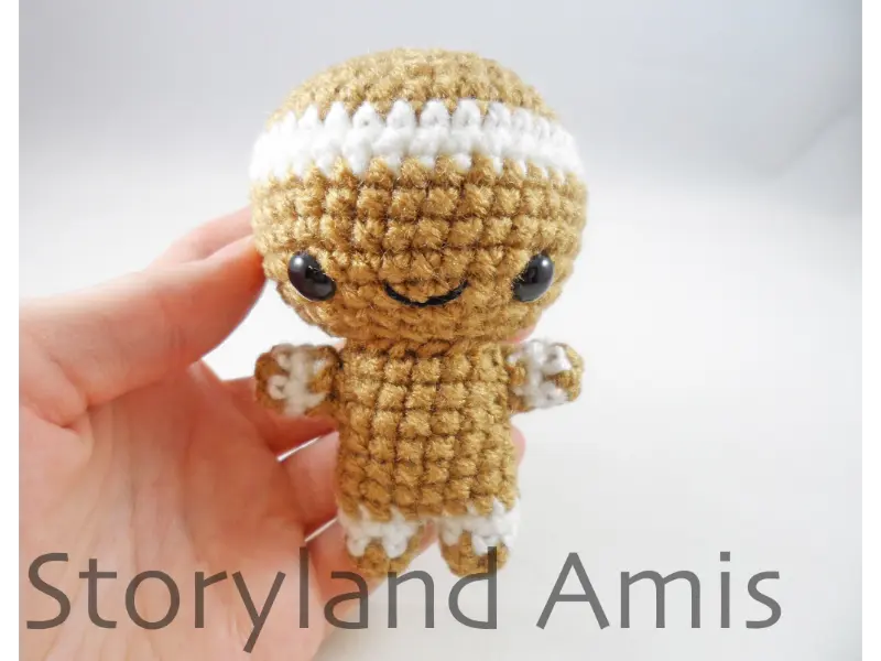 A hand holds up a partially finished amigurumi gingerbread boy.