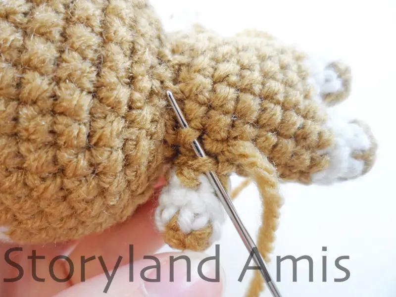 A close-up of a crocheted arm being sewn to an amigurumi gingerbread boy's body with a silver tapestry needle.