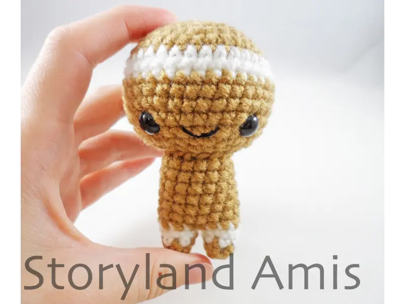 A hand holds up a partially finished amigurumi gingerbread boy.
