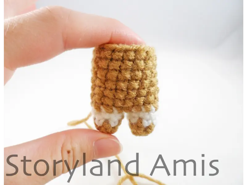 A hand holds up a completed amigurumi body for a mini gingerbread boy.