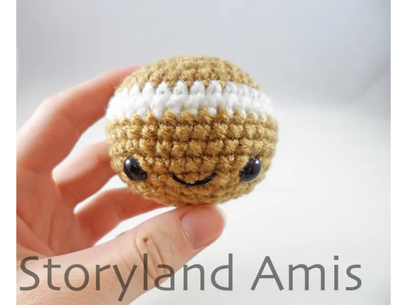A hand holds a small crocheted gingerbread man head.
