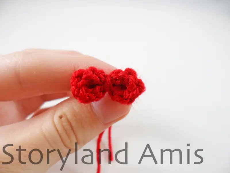 A hand holds up a small red crocheted bow.