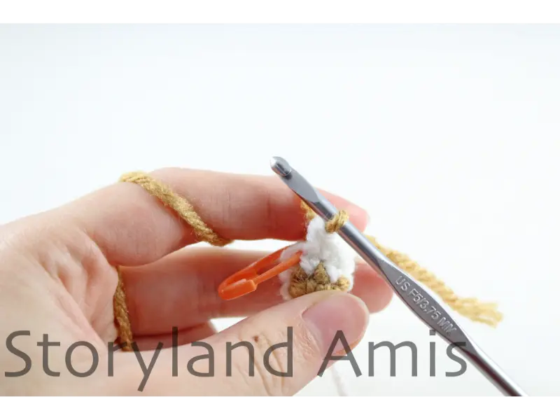 A hand holds up a crocheted gingerbread boy's foot. A silver crochet hook is inserted into a stitch on the leg.