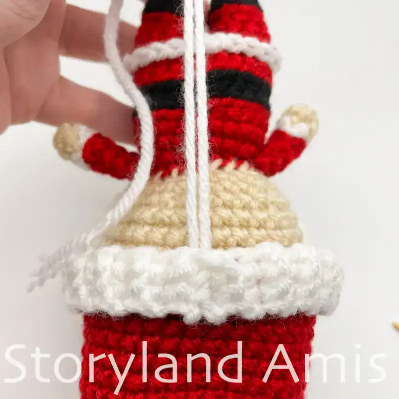 The backside of a crocheted Santa Claus doll is shown upside down. Two yarn tails extend from the hat band.